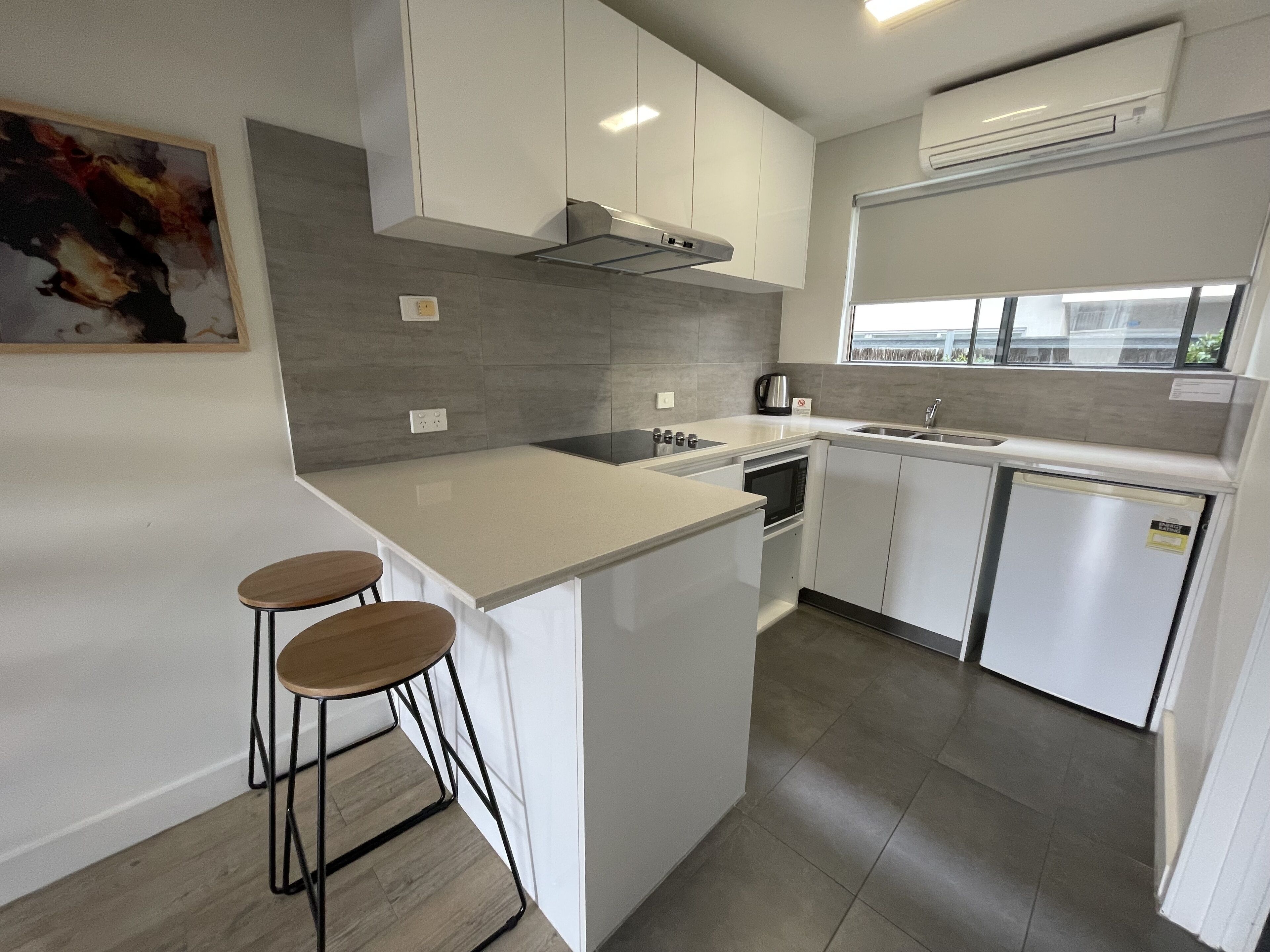 A modern kitchen with white cabinetry, a central island with stools, a built-in oven, and a window above the sink.