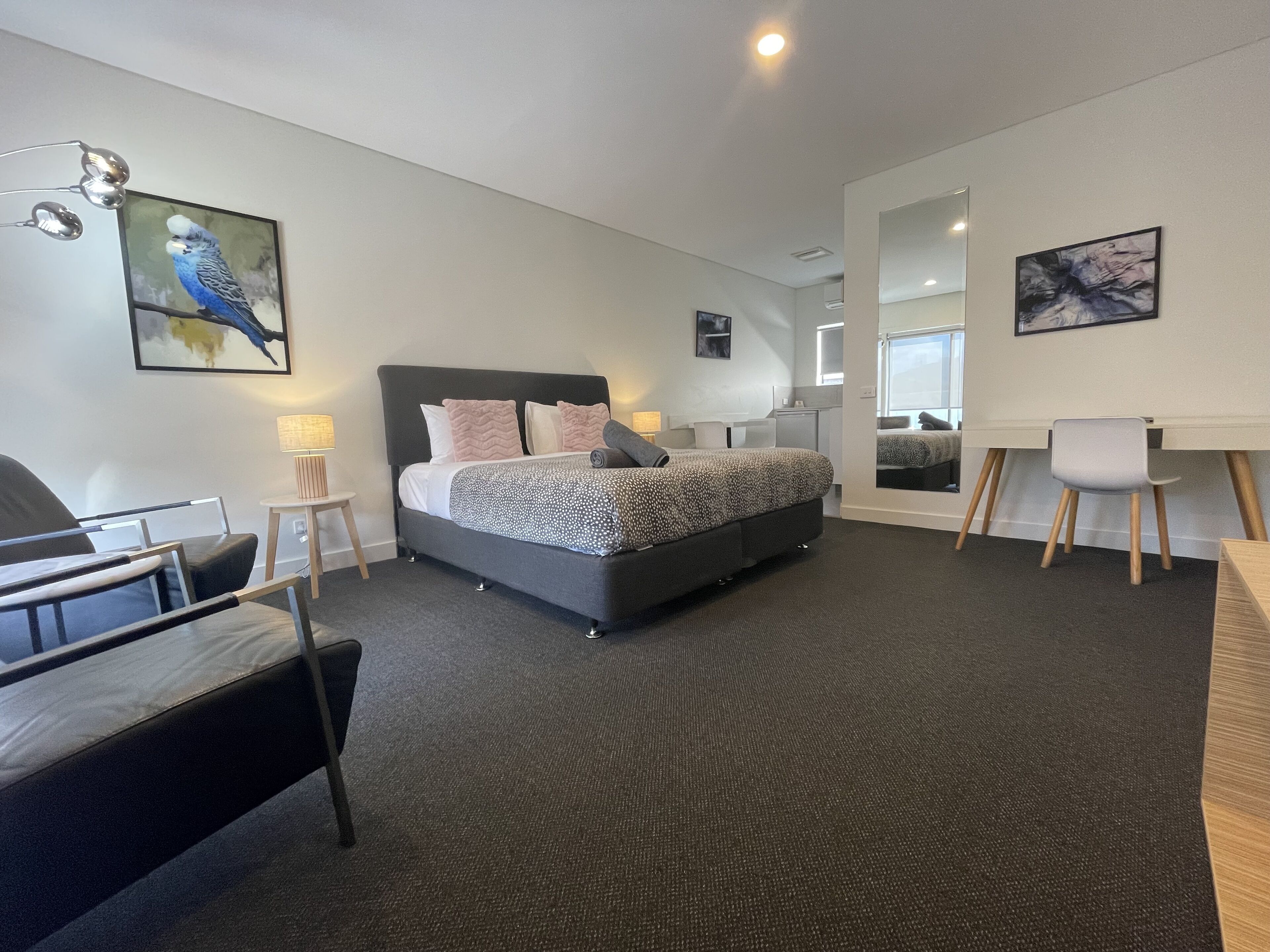 A modern bedroom with a large bed, a desk, and a chair. There are wall-mounted lamps and artwork.