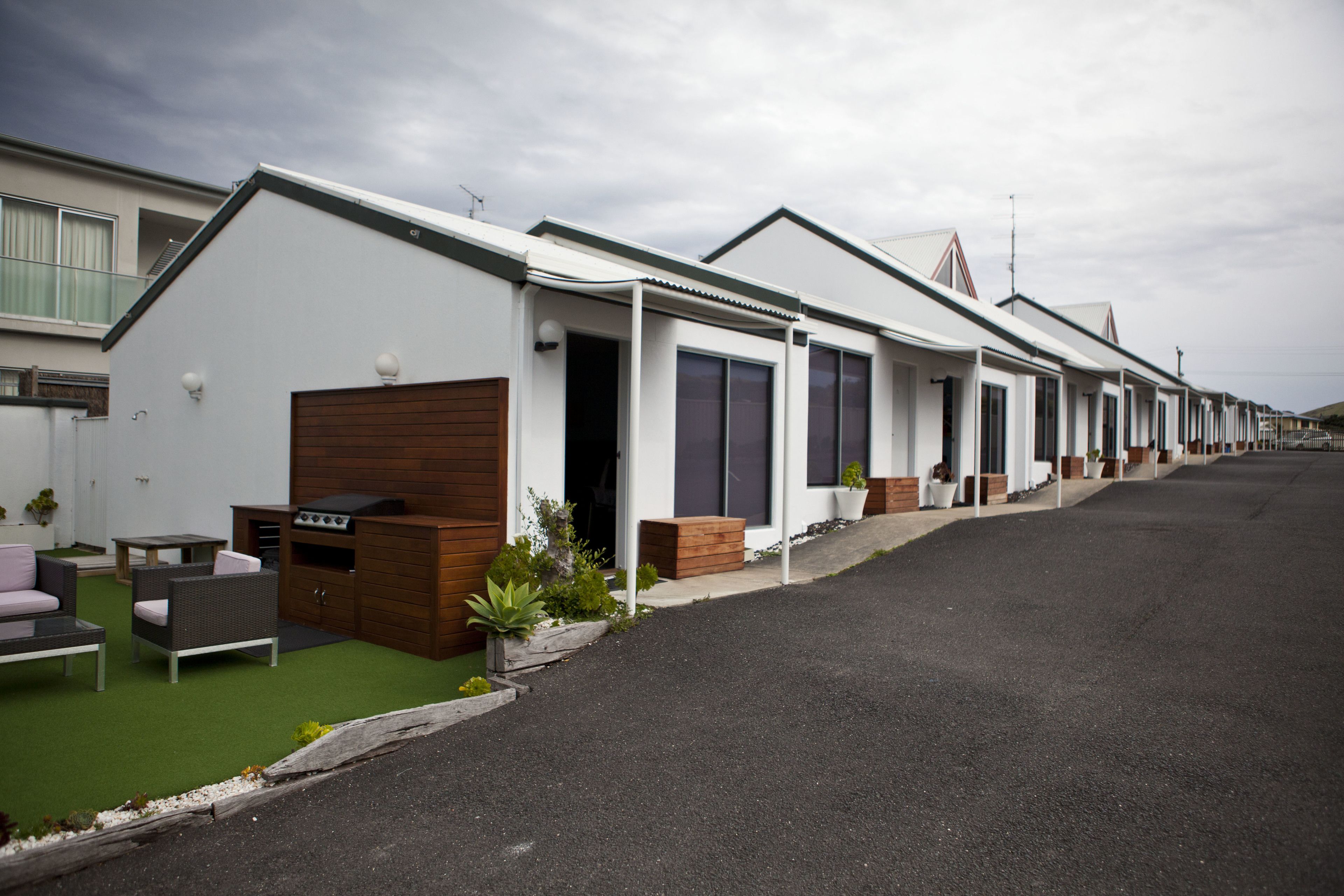 Une rangée de maisons mobiles modernes, dotées d’un toit plat, d’un petit patio avec du mobilier d’extérieur et d’une allée pavée.