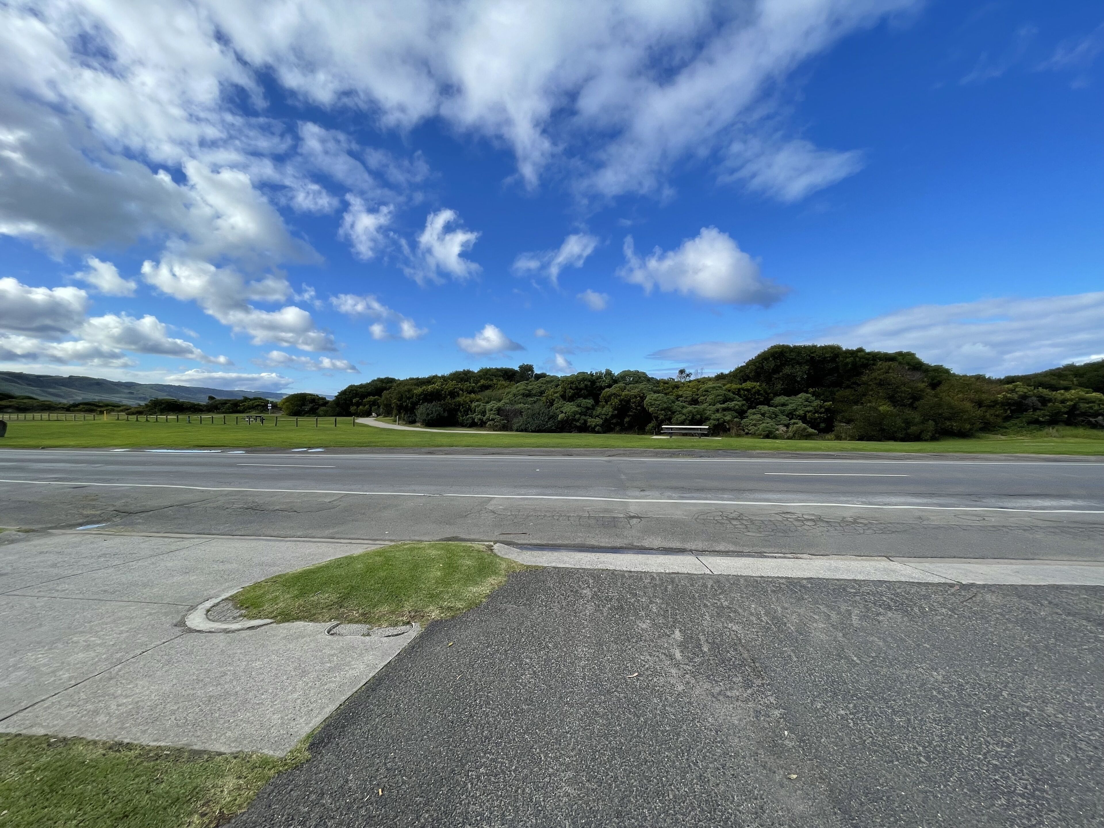 A road leading to a park with a bench and a grassy area.