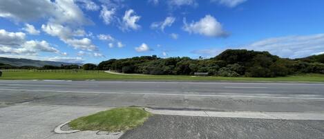 A road leading to a park with a bench and a grassy area.
