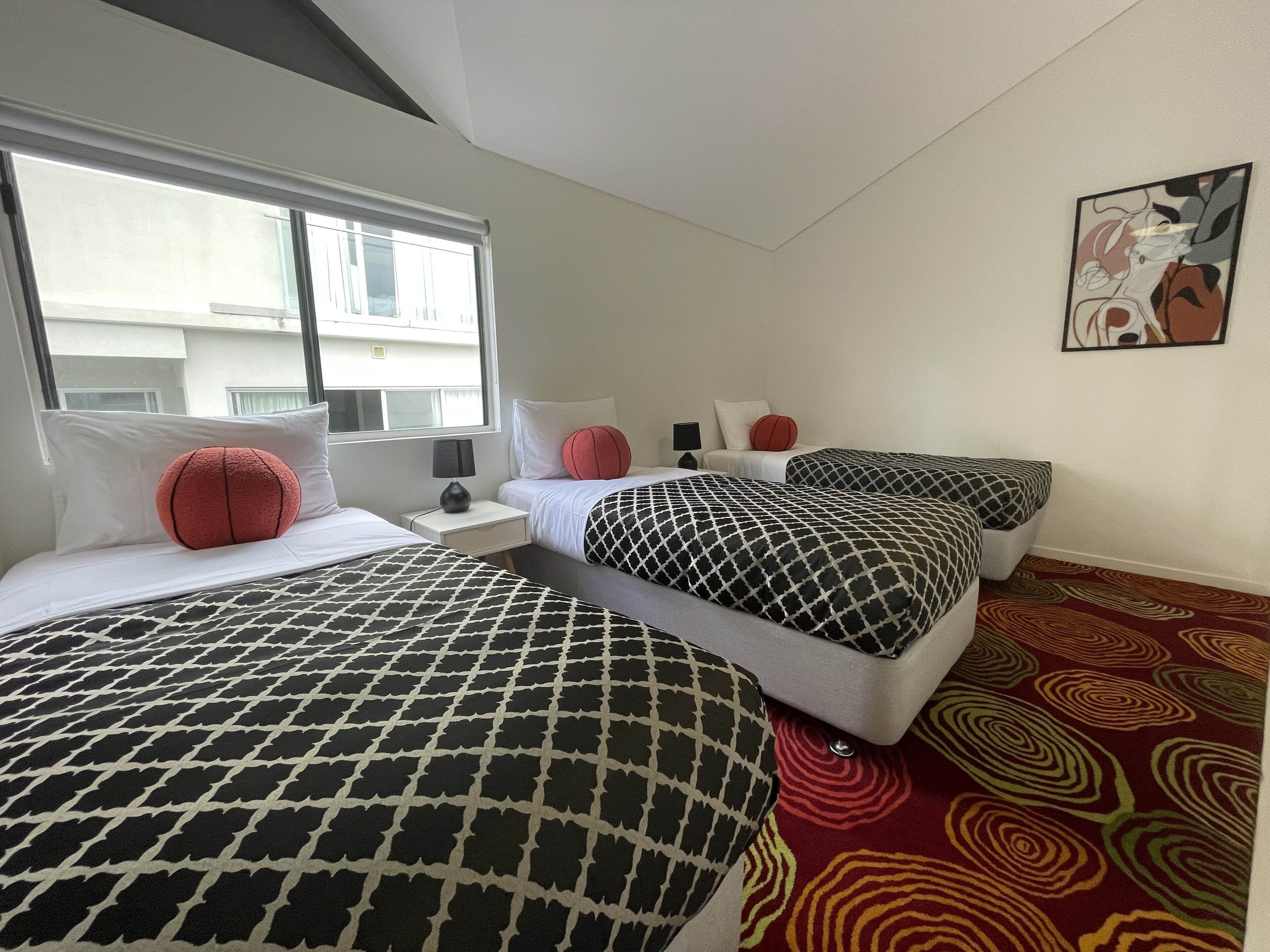 A hotel room with two beds, a window, a nightstand, a lamp, and a patterned carpet.