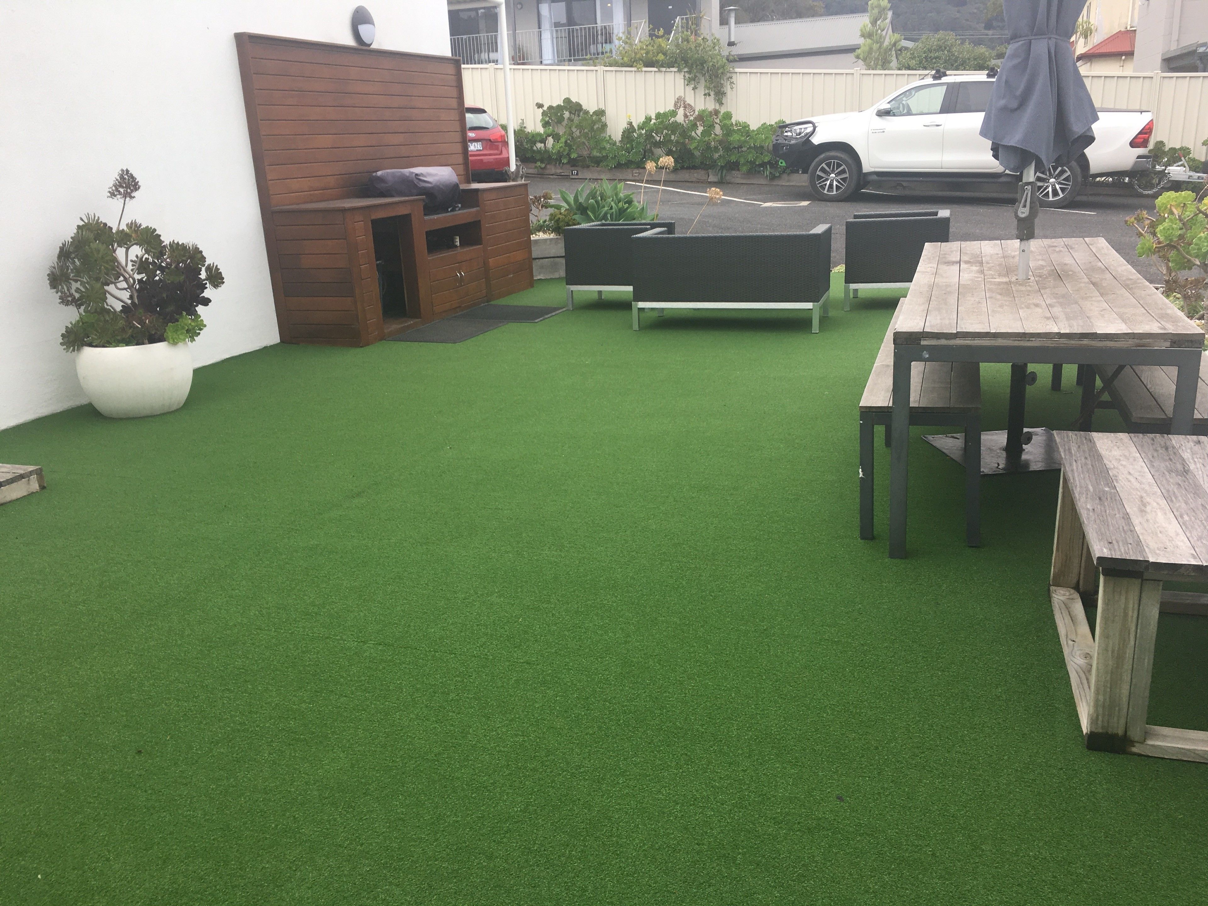 A patio with artificial grass, wooden benches, and a table.