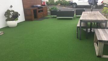 A patio with artificial grass, wooden benches, and a table.