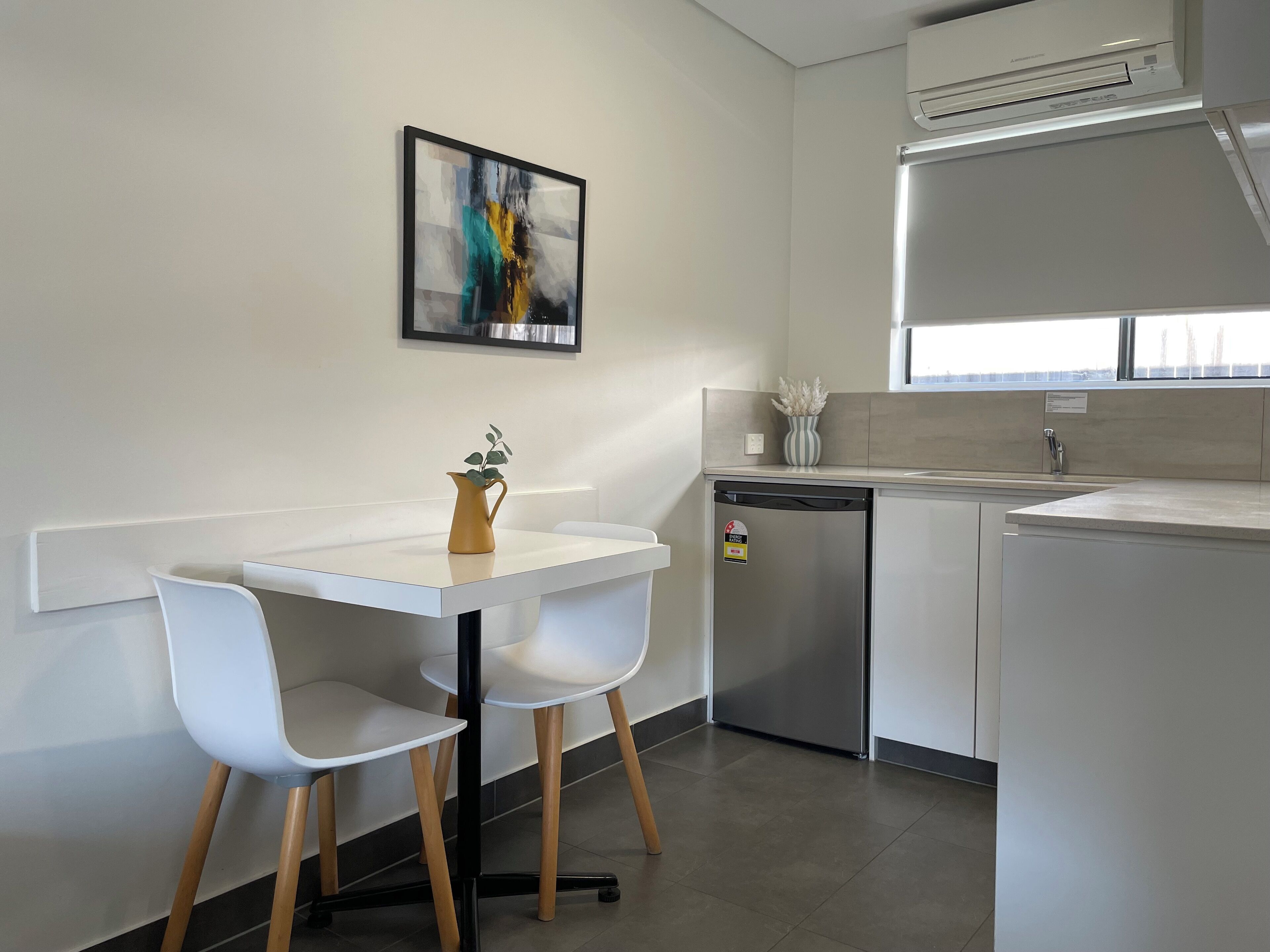 A modern kitchen with a white countertop, two white chairs, a small table, a dishwasher, and a window above the sink.