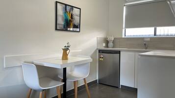 A modern kitchen with a white countertop, two white chairs, a small table, a dishwasher, and a window above the sink.