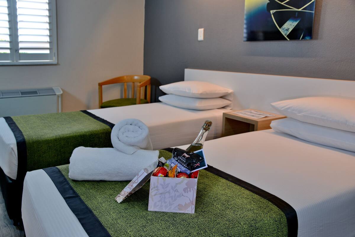 A hotel room with two beds, a wooden chair, a bottle of champagne, and a small gift box.