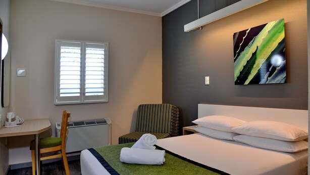 A hotel room with a bed, a desk, a chair, a radiator, and a window. - Road Lodge Umhlanga Ridge (Umhlanga)