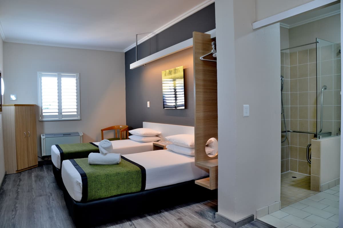 A modern hotel room with two beds, a shower area, and a view of the outdoors.