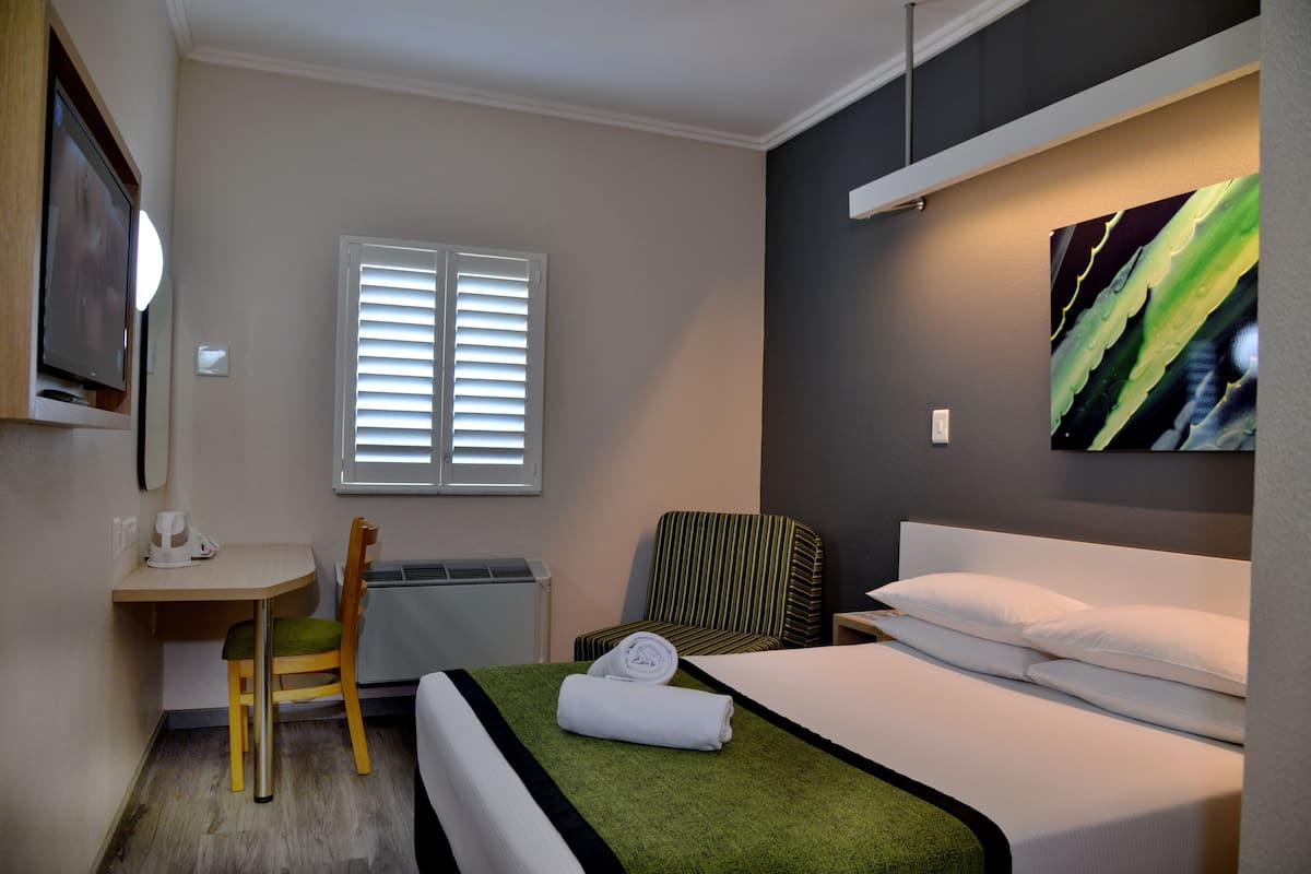 A hotel room with a bed, a desk, a chair, a TV, and a window with blinds.