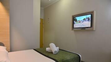 Ein Hotelzimmer mit einem Bett, einem an der Wand befestigten Fernseher und einem zusammengerollten Handtuch auf dem Bett.