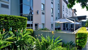 Un edificio moderno con un balcone, immerso nel verde e piante tropicali.