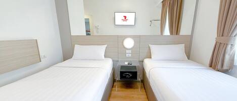 A hotel room with two single beds, a bedside table with a phone and a remote control, a mirror, and a window with curtains.