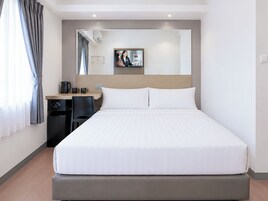 Hotellihuone, jossa on suuri sänky, työpöytä tuolilla, kahvinkeitin ja peili seinällä.