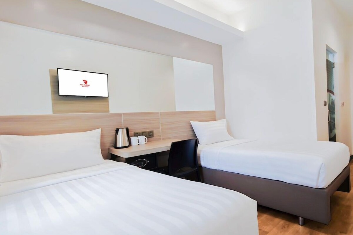 A hotel room with two beds, a desk with a coffee maker, and a TV mounted on the wall.