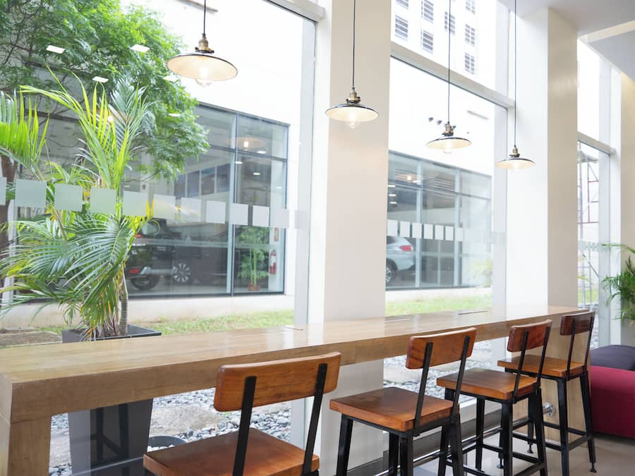 Un interior moderno con una barra de madera larga, múltiples sillas, lámparas colgantes y amplias ventanas con vistas al exterior.