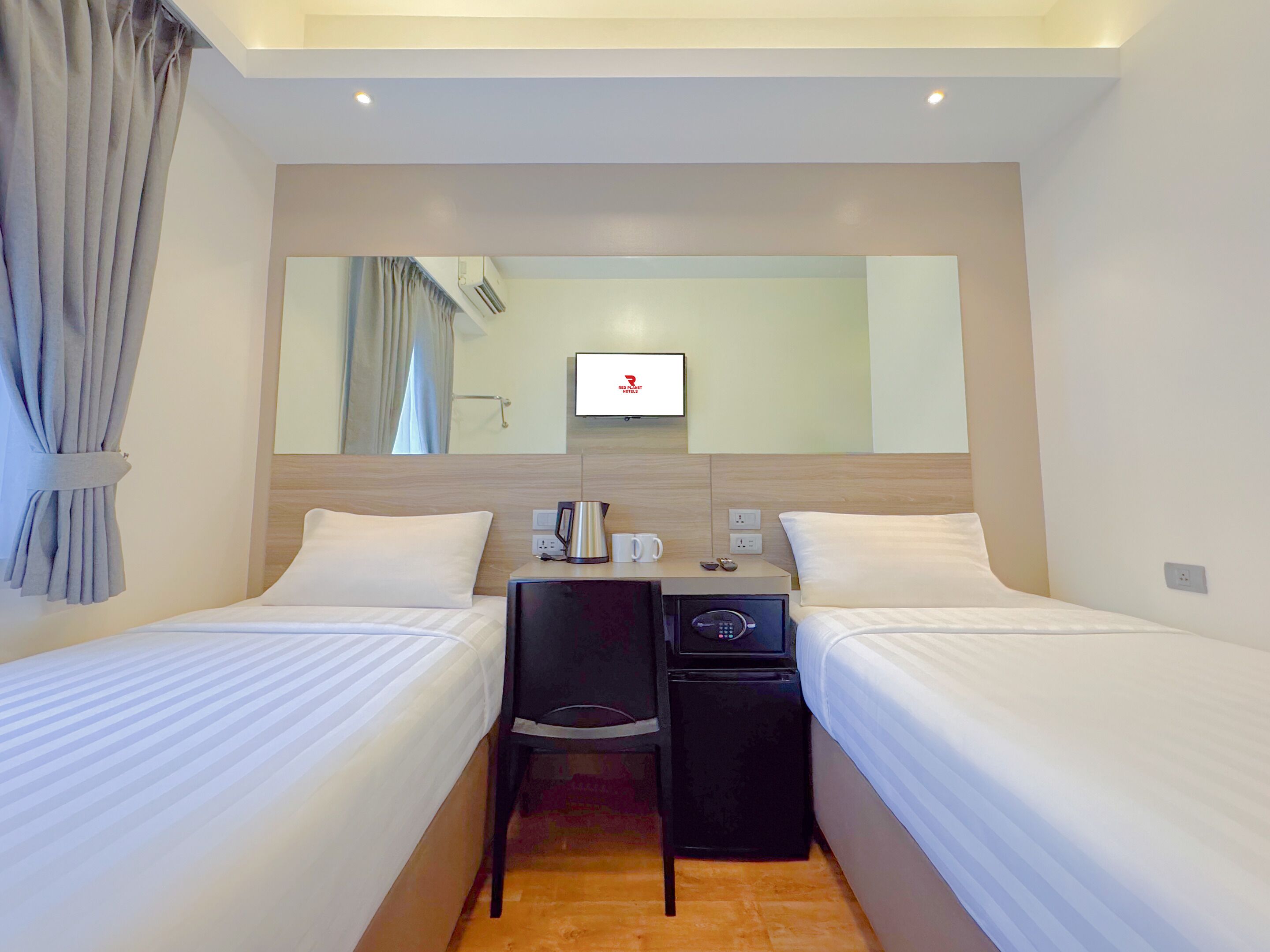 A hotel room with two single beds, a desk with a chair, a TV, and a minibar.