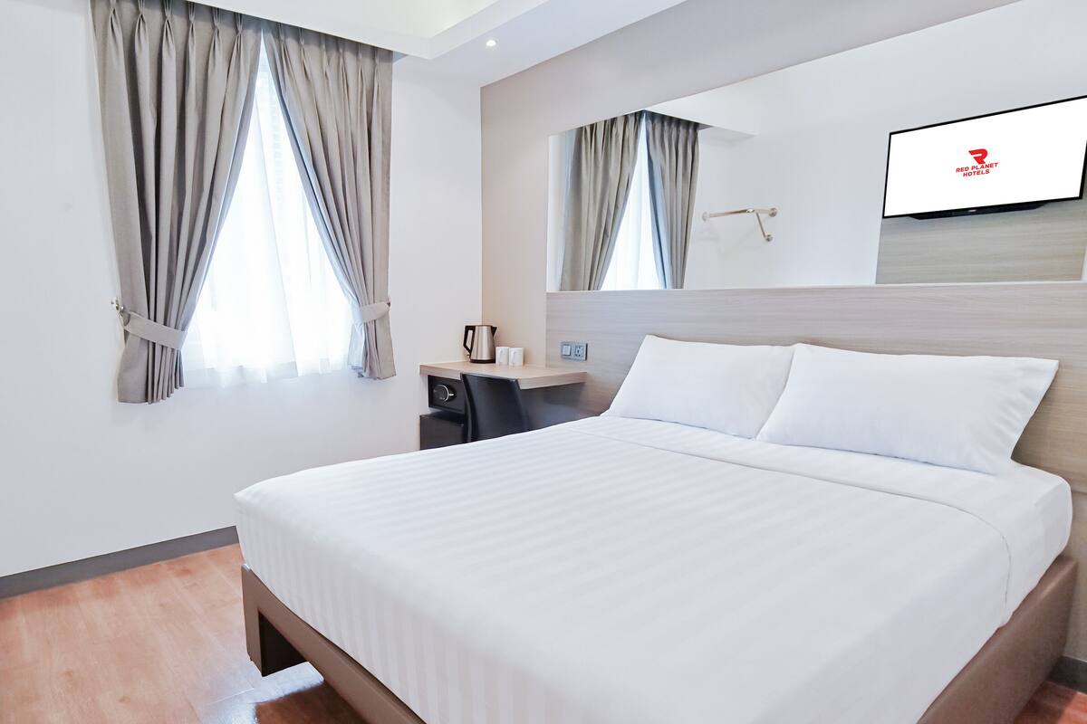 A hotel room with a large bed, a desk, a chair, a coffee maker, and a TV mounted on the wall.