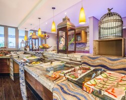 Zona de bufé con diversas opciones de comida, una jaula de pájaros decorativa de gran tamaño y lámparas colgantes.