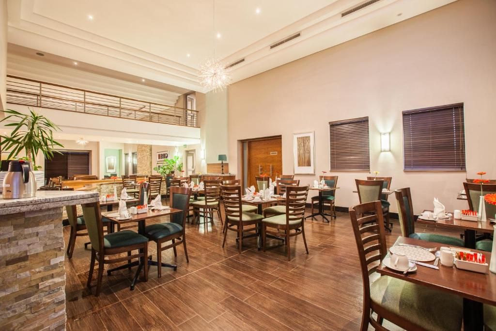 A hotel dining area with multiple tables and chairs, a kitchen in the background, and a balcony.