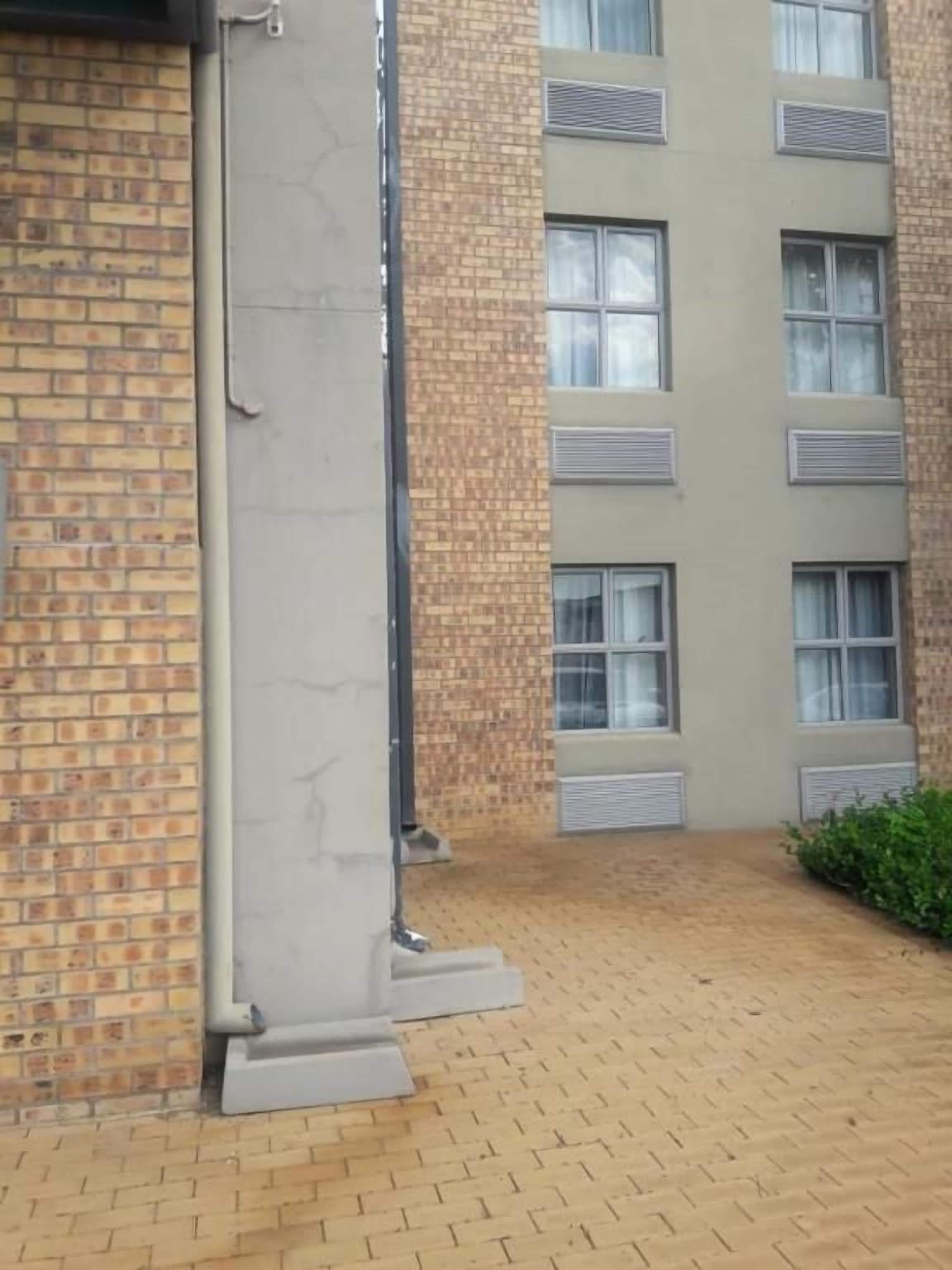 A building with a brick facade, multiple windows with air conditioning units, and a paved courtyard.