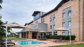 A hotel with a swimming pool, outdoor seating, and a brick facade.