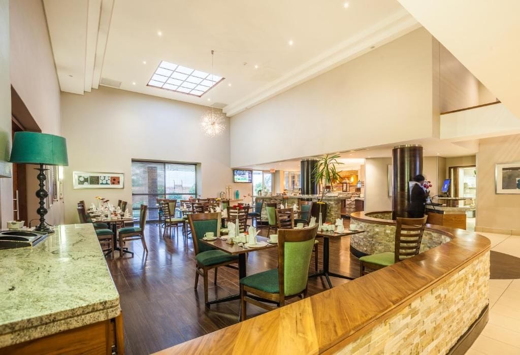 A spacious hotel lobby with a reception desk, seating area, and a large window providing natural light.