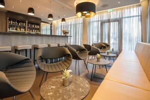 Zona de bar moderna con asientos, incluyendo mesas redondas y bancos acolchados, y una barra con diferentes botellas.