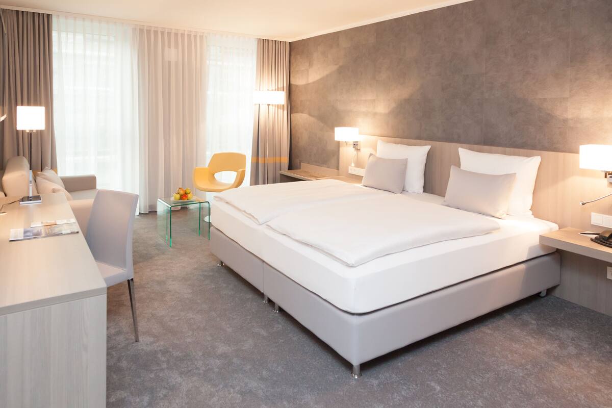 A modern hotel room with a large bed, a desk, a chair, and a small table with fruit.