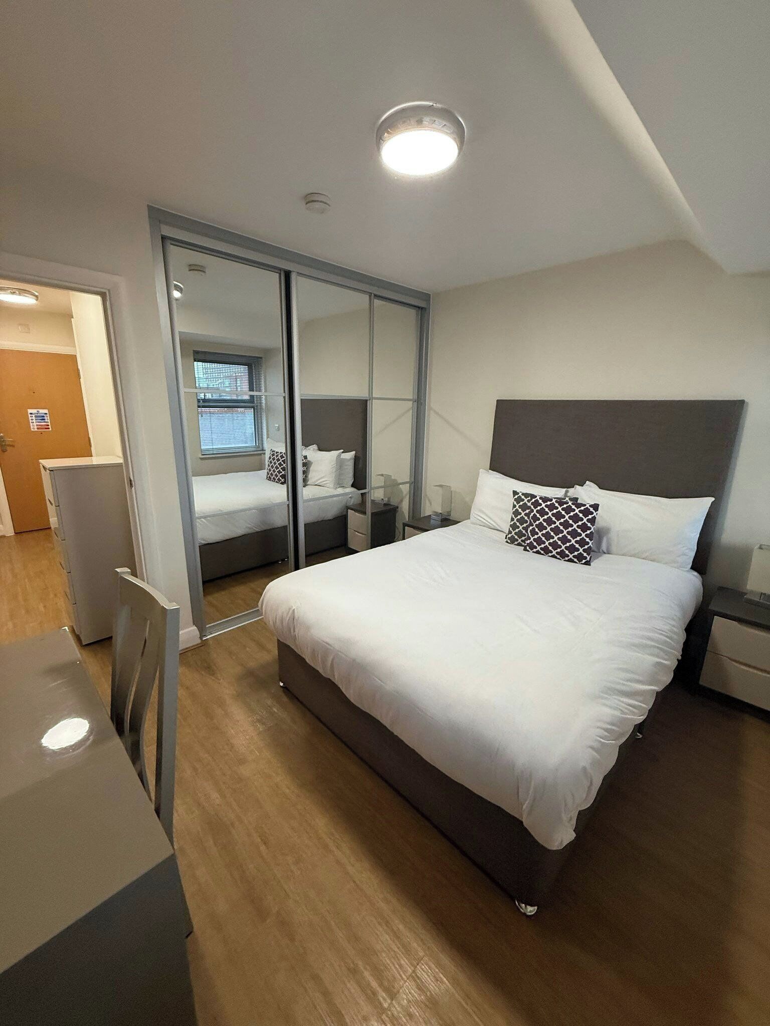 A modern bedroom with a large bed, a desk, and a mirror.