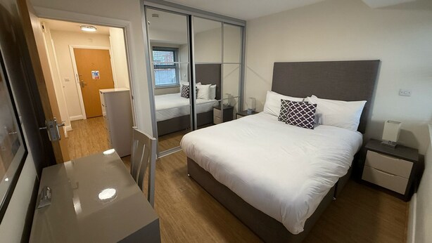 Una habitación de hotel moderna con una cama grande, un escritorio, una silla y un armario.