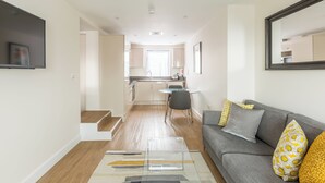 Una sala de estar moderna con un sofá gris, una mesa de centro y una cocina al fondo.