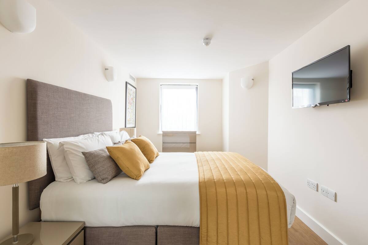 Ein modernes Hotelzimmer mit Bett, Nachttisch, Lampe und einem an der Wand befestigten Fernseher.