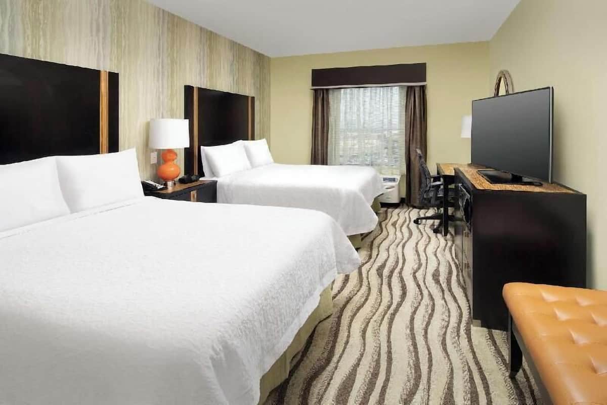 Habitación de hotel con dos camas, un escritorio con computadora, televisión y ventana con cortinas.