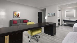 Une chambre d’h ôtel moderne, dotée d’un grand bureau, d’un canapé avec des coussins rouges, d’un fauteuil de bureau jaune, d’une console noire et d’un grand miroir.