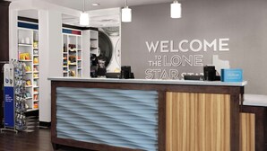 Un comptoir d’accueil d’hôtel avec une pancarte indiquant « Bienvenue au Lone Star », un minibar et une pancarte « Hilton Honors ».