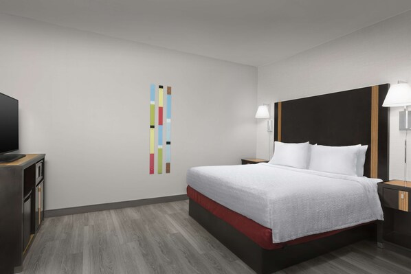 A hotel room with a bed, bedside tables, a TV, and a colorful wall decoration.