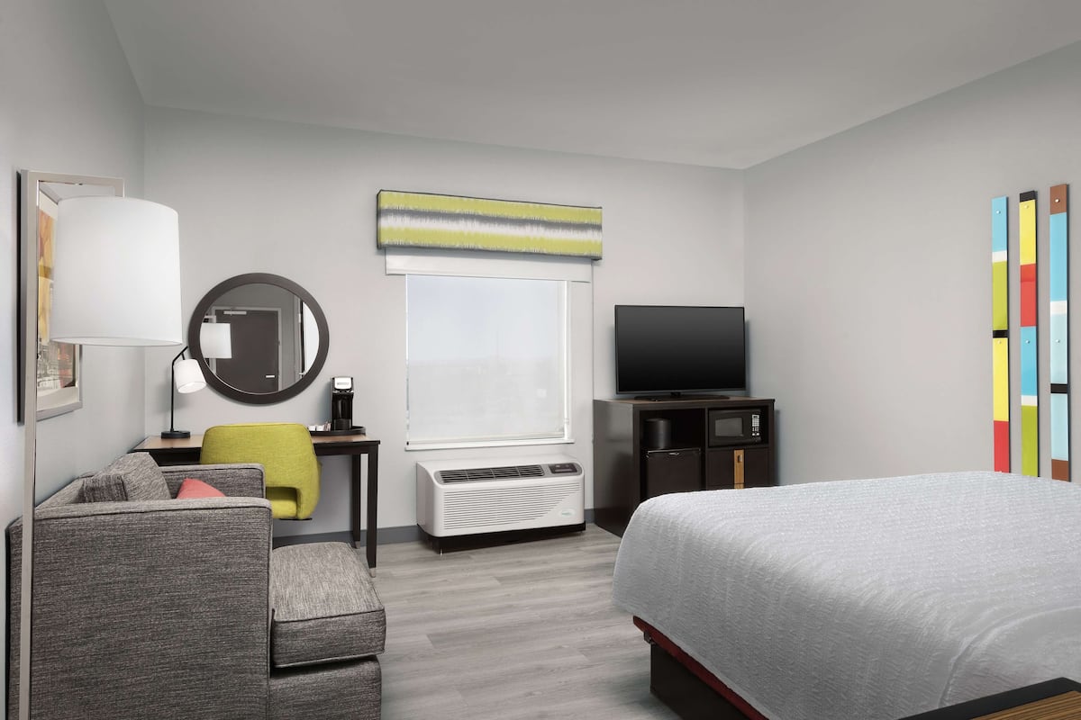 Habitación de hotel con cama, escritorio, silla, televisor, espejo y ventana.