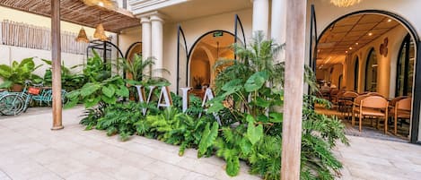 A spacious outdoor area with a tiled floor, surrounded by lush green plants and wooden columns.