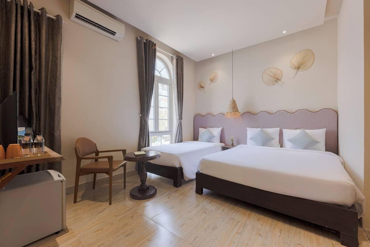 Una habitación de hotel con dos camas, un escritorio con silla, una mesita y un refrigerador.