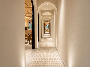 Un couloir doté d’un sol à motifs, de plafonds en arc de cercle et d’une vue sur une salle à manger avec des tables et des chaises.