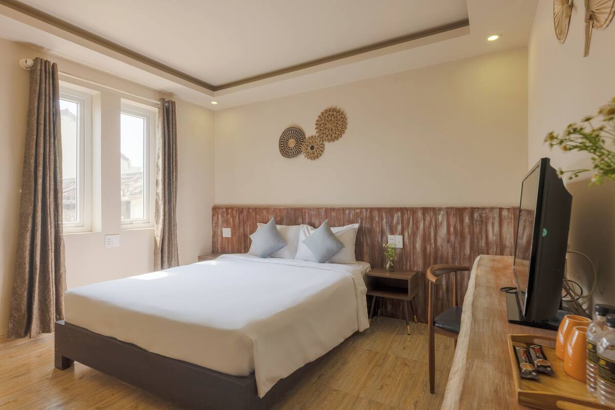 Habitación de hotel con una cama grande, cabecera de madera, dos elementos decorativos en la pared, un escritorio con silla y un televisor.