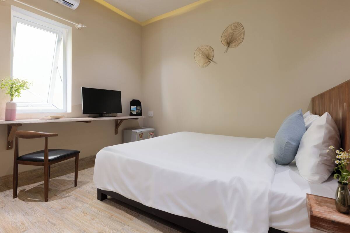 Un dormitorio con cama, escritorio, computadora, silla y ventana.