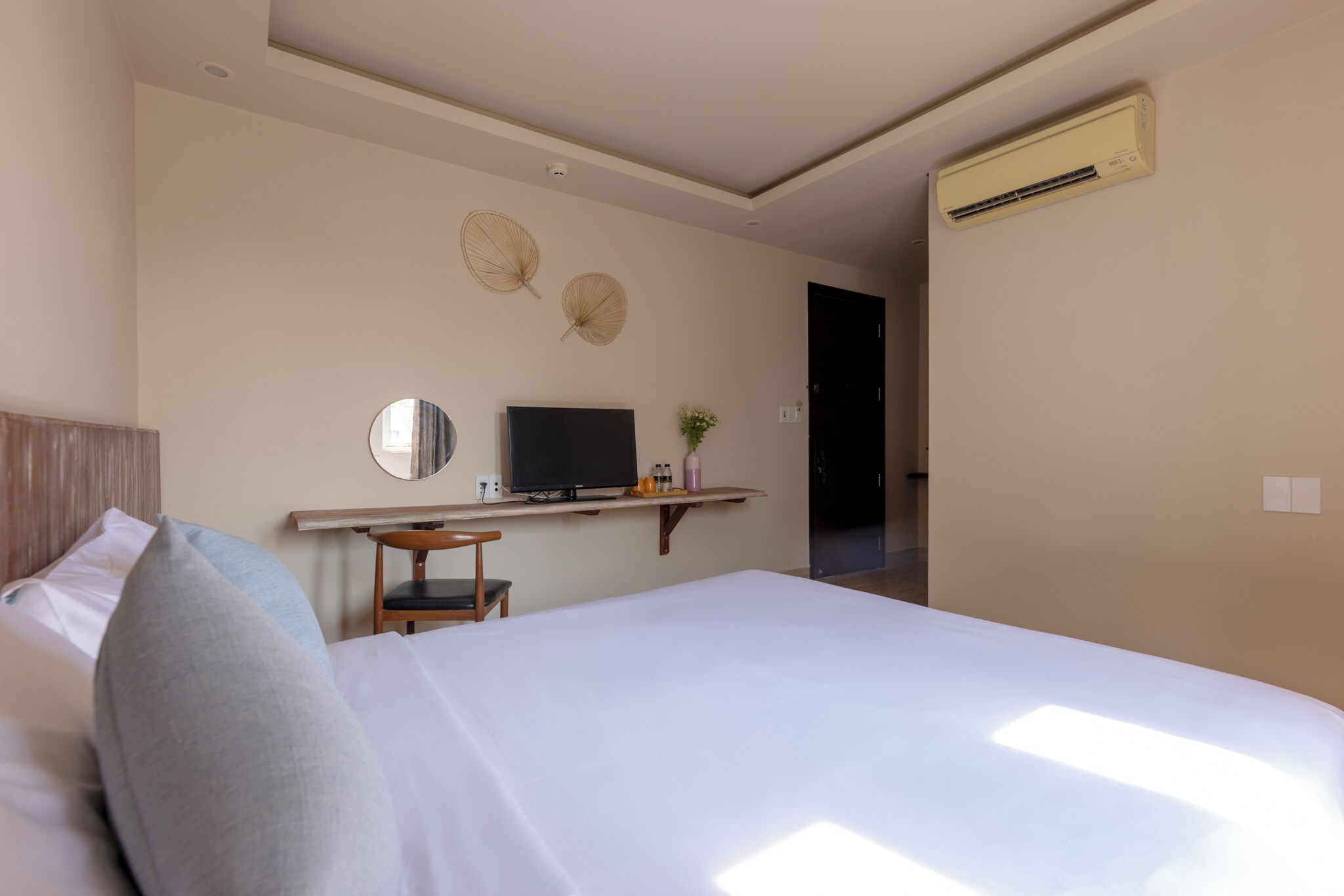 A hotel room with a bed, a desk with a computer, a television, and an air conditioning unit.