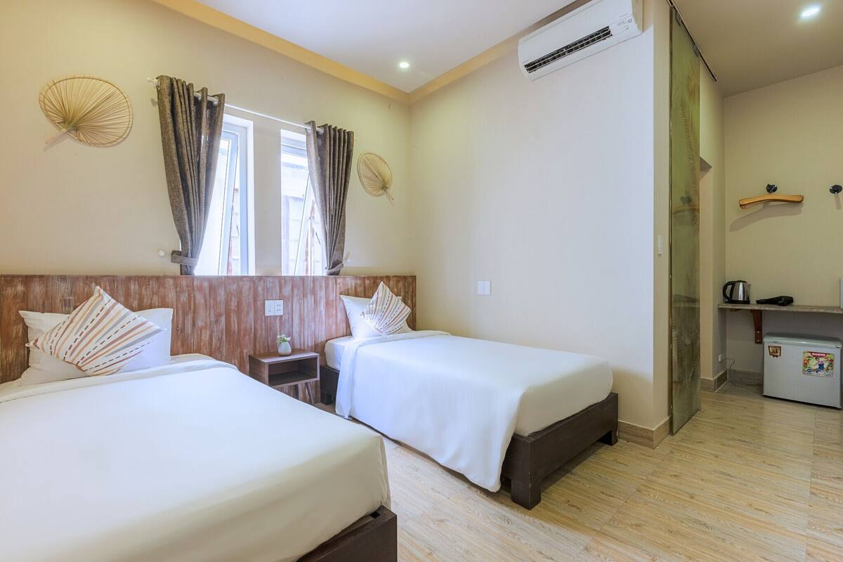 Habitación de hotel con dos camas, un escritorio pequeño, un refrigerador y una ventana con cortinas.