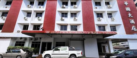 A hotel with a red and white facade, multiple air conditioning units, and a covered entrance.