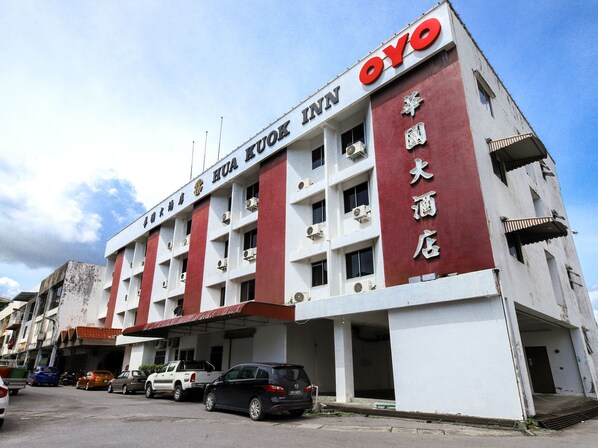 A multi-story building with the signage "HUA FOOK INN" and "OYO" indicating a hotel. There are several parked cars in front, and the building has multiple balconies.