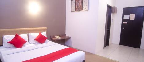 Quarto de hotel com uma cama grande, uma mesa de cabeceira com telefone, uma obra de arte na parede e uma porta com placa.