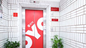 A red elevator with a white arrow symbol, surrounded by white tiled walls and two potted plants. - Hotel O Hua Kuok Inn (Kuching)