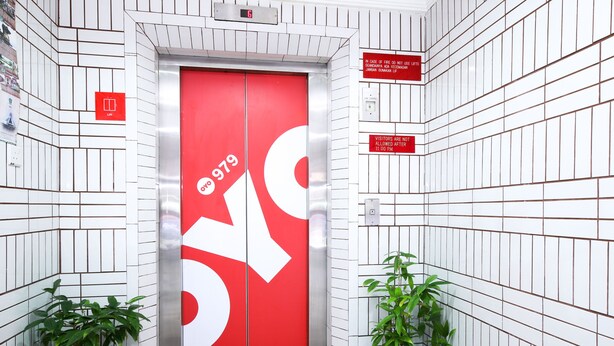 A red elevator with a white arrow symbol, surrounded by white tiled walls and two potted plants. - Hotel O Hua Kuok Inn (Kuching)